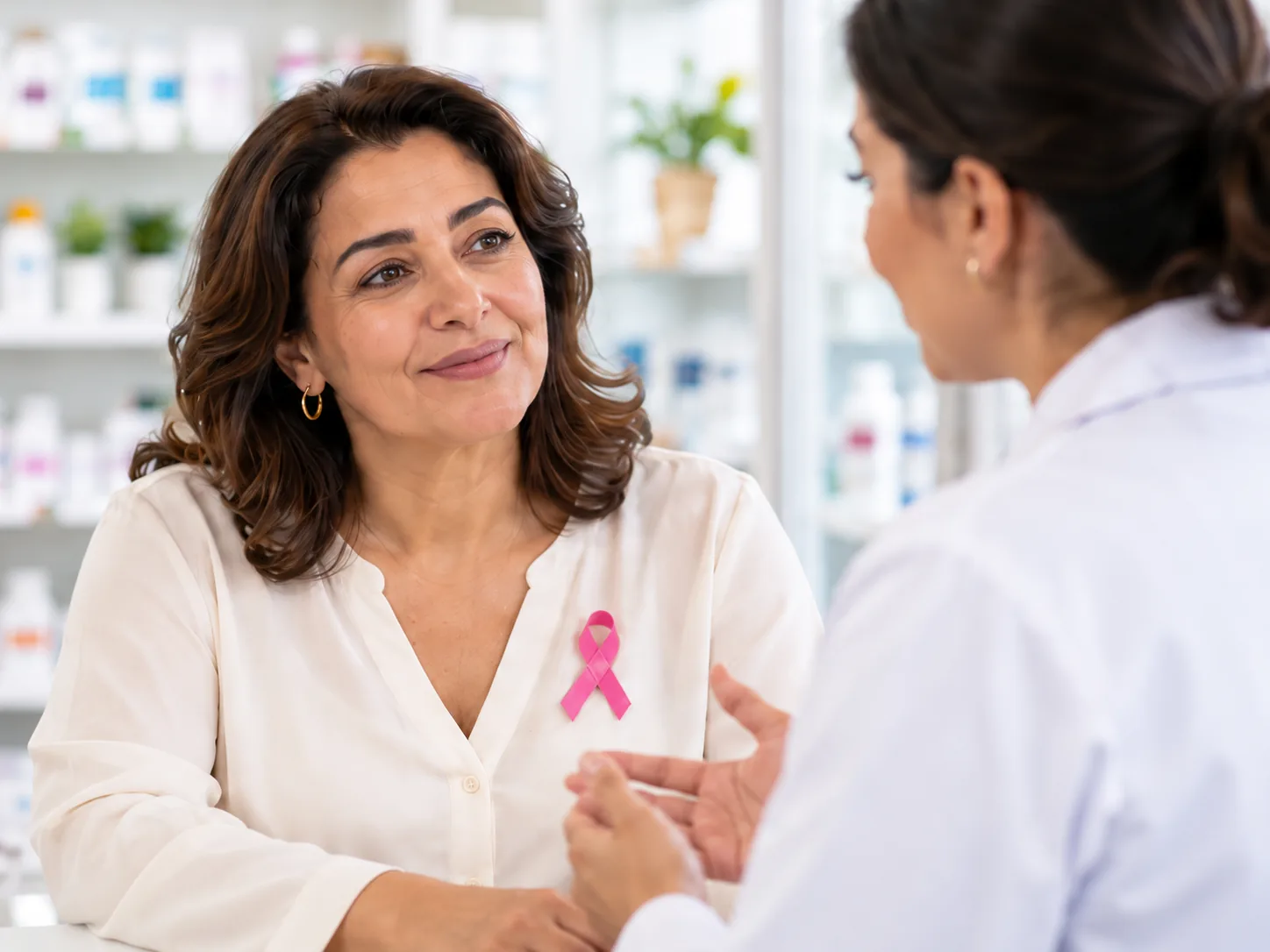 Femme portant un ruban rose en conversation avec une pharmacienne.